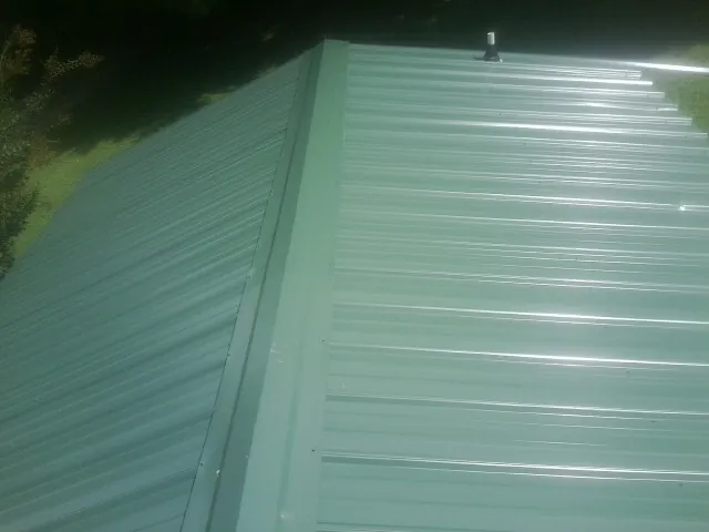 New green metal panels meeting at the ridge of a roof — Flat Roof Repair work by our crew in Fort White