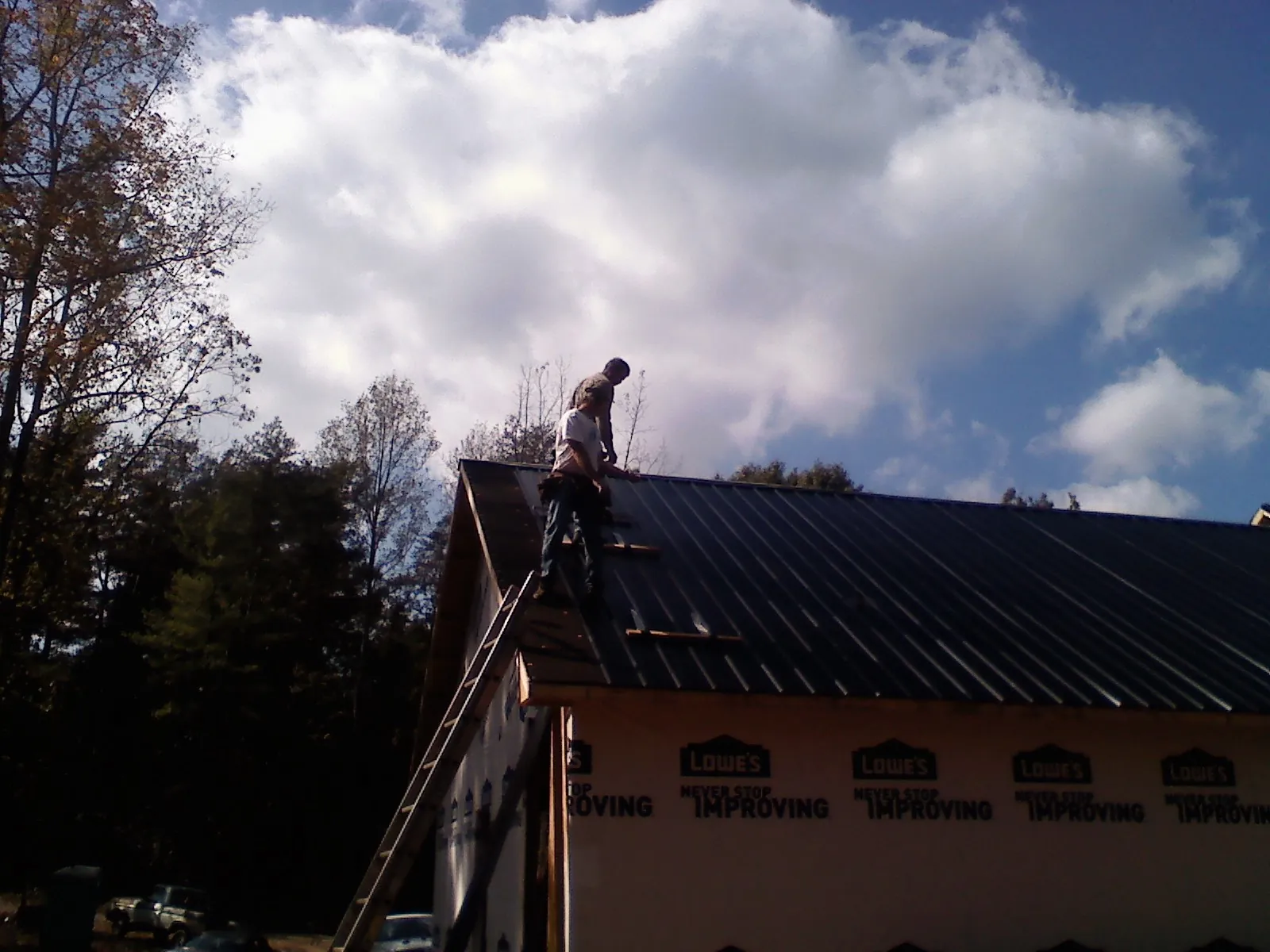 Roofer fastening dark metal panels high against a cloudy sky, from a Roof Inspection job in Fort White