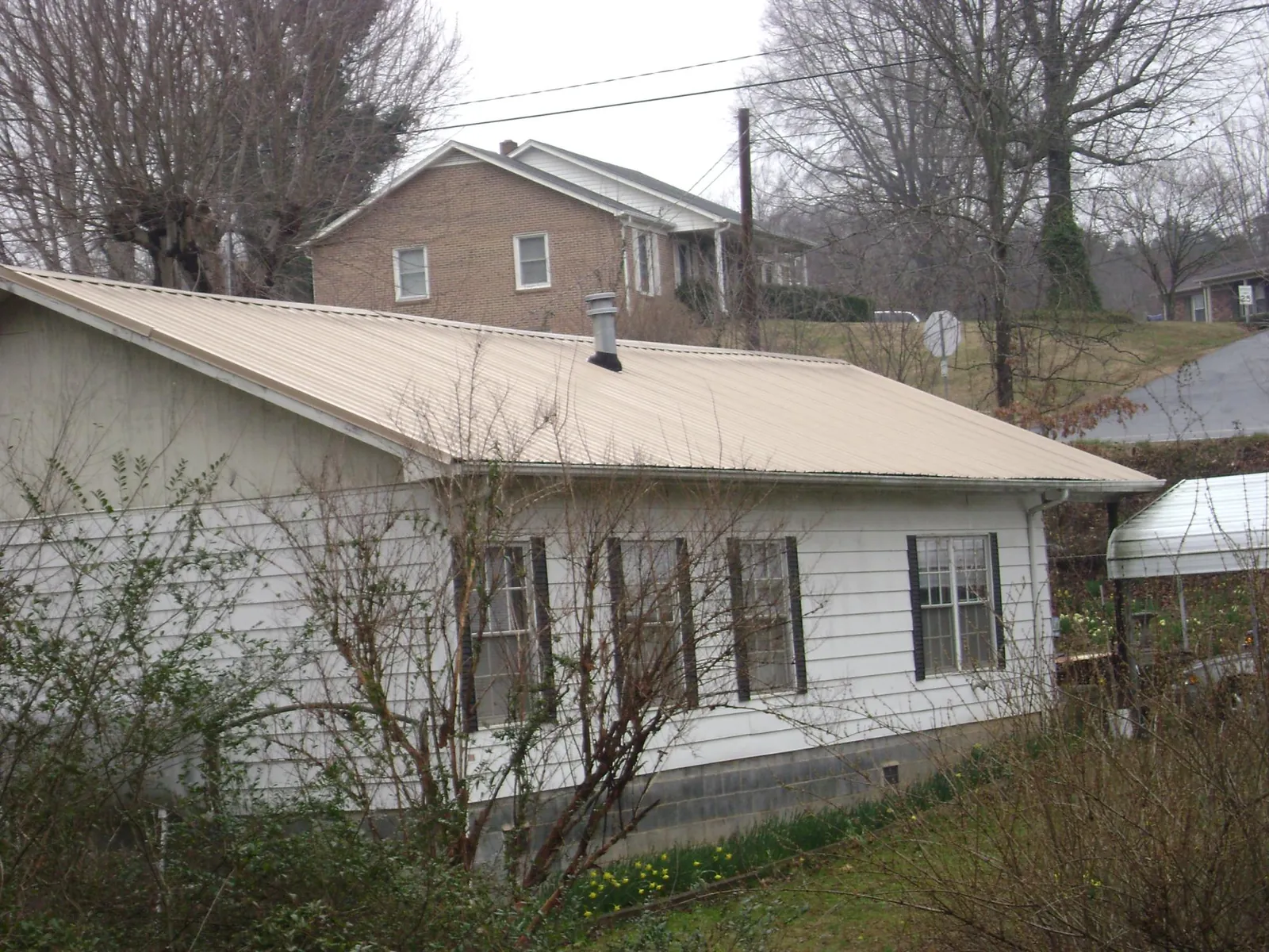 Tan metal roof on a white sided house set into a hillside — Commercial Roofing by Roofing Brothers in Fort White