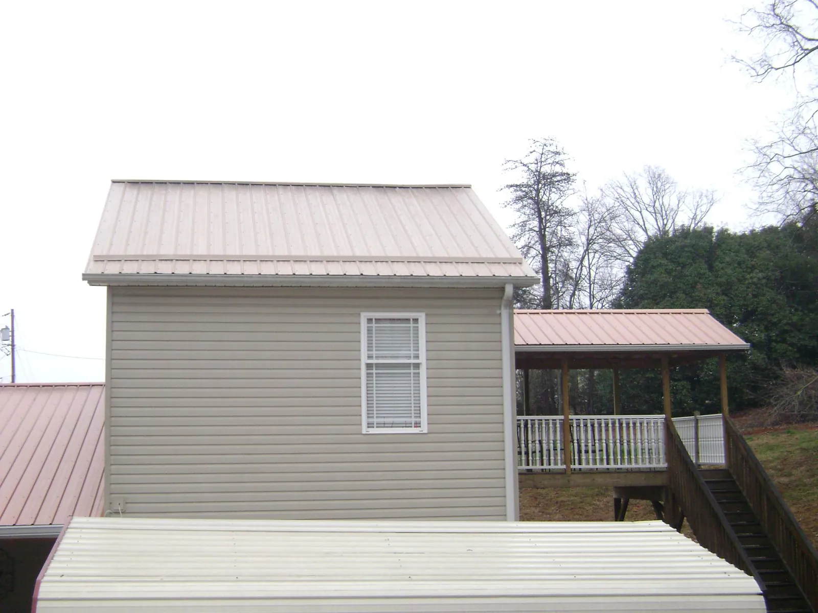 Tan metal roofs on a two story addition and attached porch, from a Roof Replacement job in Fort White